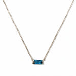 A December Birthstone Aqua Cubic Zirconia Baguette Necklace by Skōsh Jewelry, featuring a slim rectangular blue baguette stone set horizontally on a fine sterling silver chain, displayed against a white background.