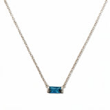 A December Birthstone Aqua Cubic Zirconia Baguette Necklace by Skōsh Jewelry, featuring a slim rectangular blue baguette stone set horizontally on a fine sterling silver chain, displayed against a white background.