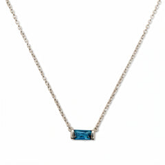 A December Birthstone Aqua Cubic Zirconia Baguette Necklace by Skōsh Jewelry, featuring a slim rectangular blue baguette stone set horizontally on a fine sterling silver chain, displayed against a white background.