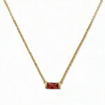 A January Birthstone Garnet Cubic Zirconia Baguette Necklace by Skōsh Jewelry, featuring a slim rectangular deep red baguette stone set horizontally on a fine gold chain, displayed against a white background.