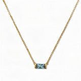 A March Birthstone Light Sapphire Cubic Zirconia Baguette Necklace by Skōsh Jewelry, featuring a slim rectangular light blue baguette stone set horizontally on a fine gold chain, displayed against a white background.