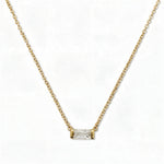 An April Birthstone White Cubic Zirconia Baguette Necklace by Skōsh Jewelry, featuring a slim rectangular clear baguette stone set horizontally on a fine gold chain, displayed against a white background.