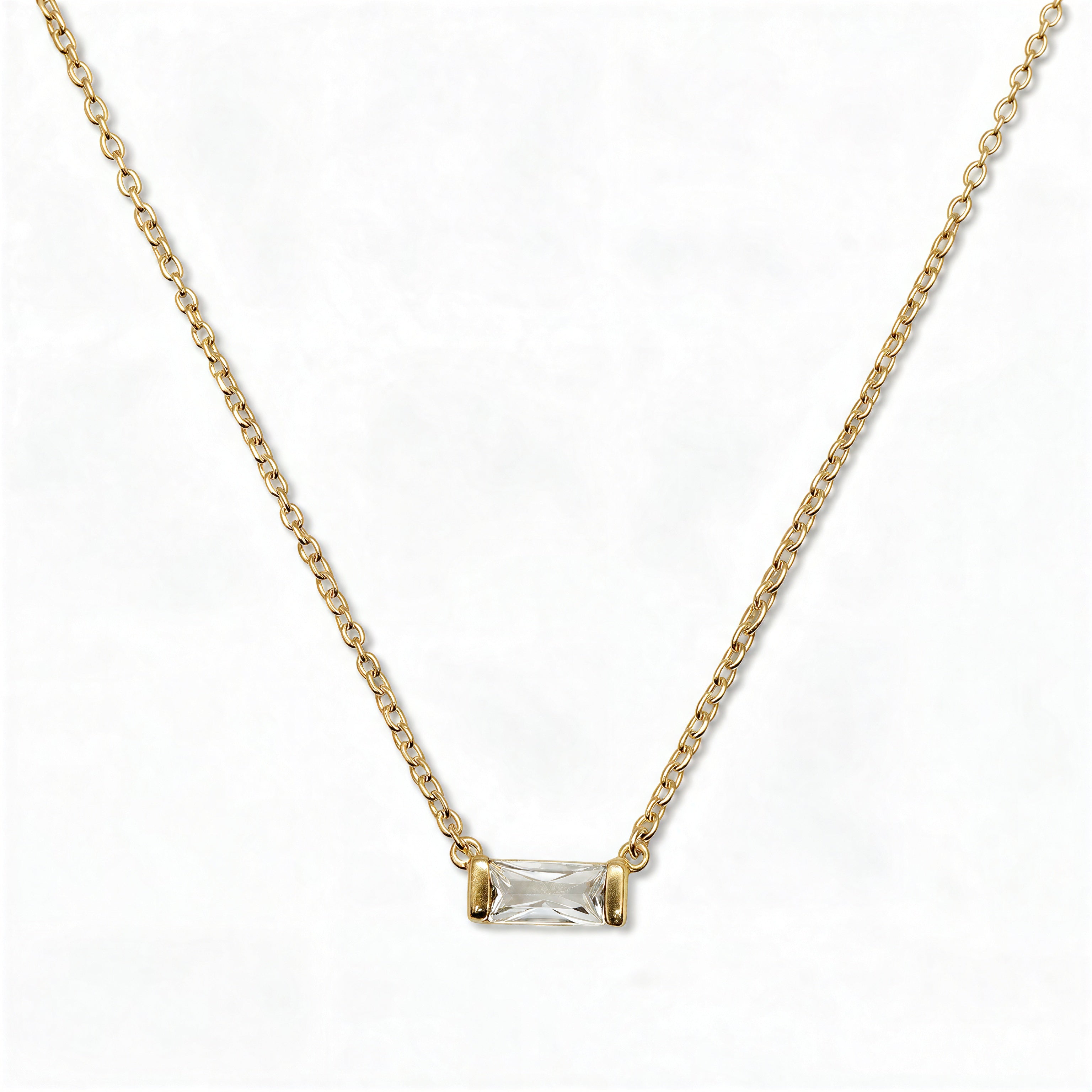 An April Birthstone White Cubic Zirconia Baguette Necklace by Skōsh Jewelry, featuring a slim rectangular clear baguette stone set horizontally on a fine gold chain, displayed against a white background.