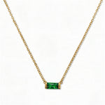 A May Birthstone Emerald Cubic Zirconia Baguette Necklace by Skōsh Jewelry, featuring a slim rectangular green baguette stone set horizontally on a fine gold chain, displayed against a white background.