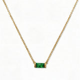 A May Birthstone Emerald Cubic Zirconia Baguette Necklace by Skōsh Jewelry, featuring a slim rectangular green baguette stone set horizontally on a fine gold chain, displayed against a white background.