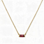 A July Birthstone Ruby Cubic Zirconia Baguette Necklace by Skōsh Jewelry, featuring a slim rectangular red baguette stone set horizontally on a fine gold chain, displayed against a white background.