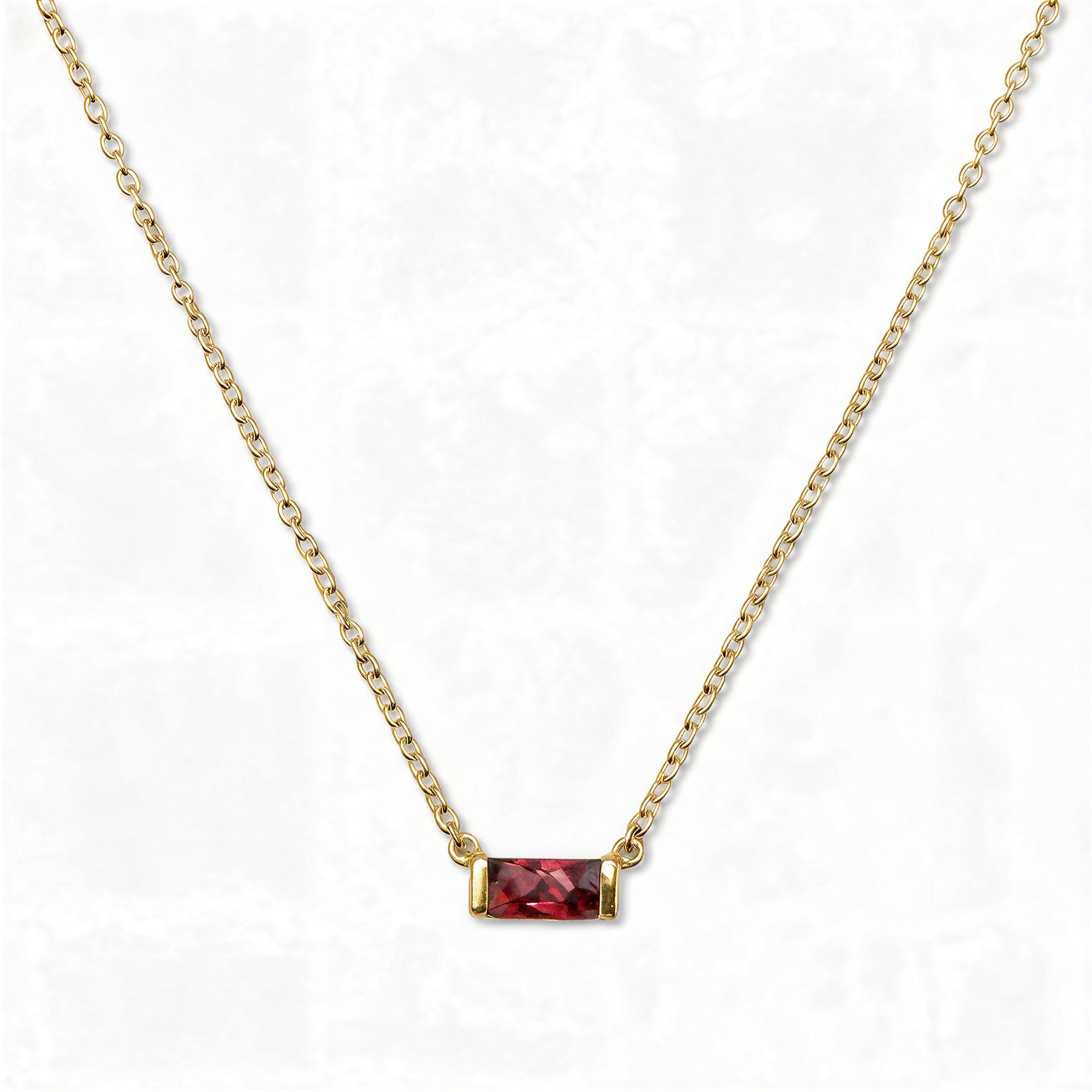A July Birthstone Ruby Cubic Zirconia Baguette Necklace by Skōsh Jewelry, featuring a slim rectangular red baguette stone set horizontally on a fine gold chain, displayed against a white background.