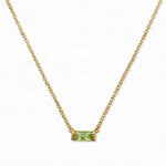 An August Birthstone Peridot Cubic Zirconia Baguette Necklace by Skōsh Jewelry, featuring a slim rectangular light green baguette stone set horizontally on a fine gold chain, displayed against a white background.