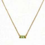 An August Birthstone Peridot Cubic Zirconia Baguette Necklace by Skōsh Jewelry, featuring a slim rectangular light green baguette stone set horizontally on a fine gold chain, displayed against a white background.