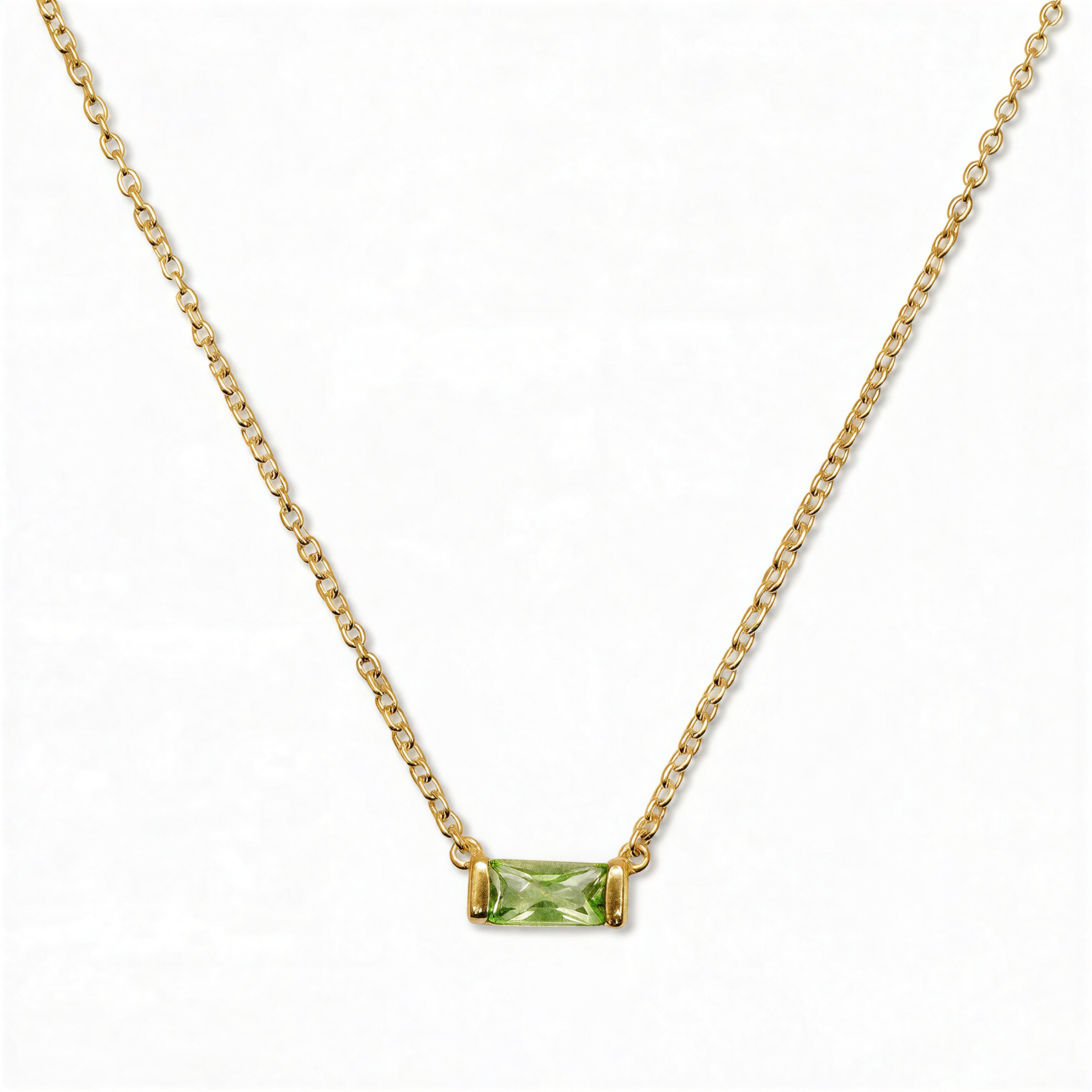 An August Birthstone Peridot Cubic Zirconia Baguette Necklace by Skōsh Jewelry, featuring a slim rectangular light green baguette stone set horizontally on a fine gold chain, displayed against a white background.