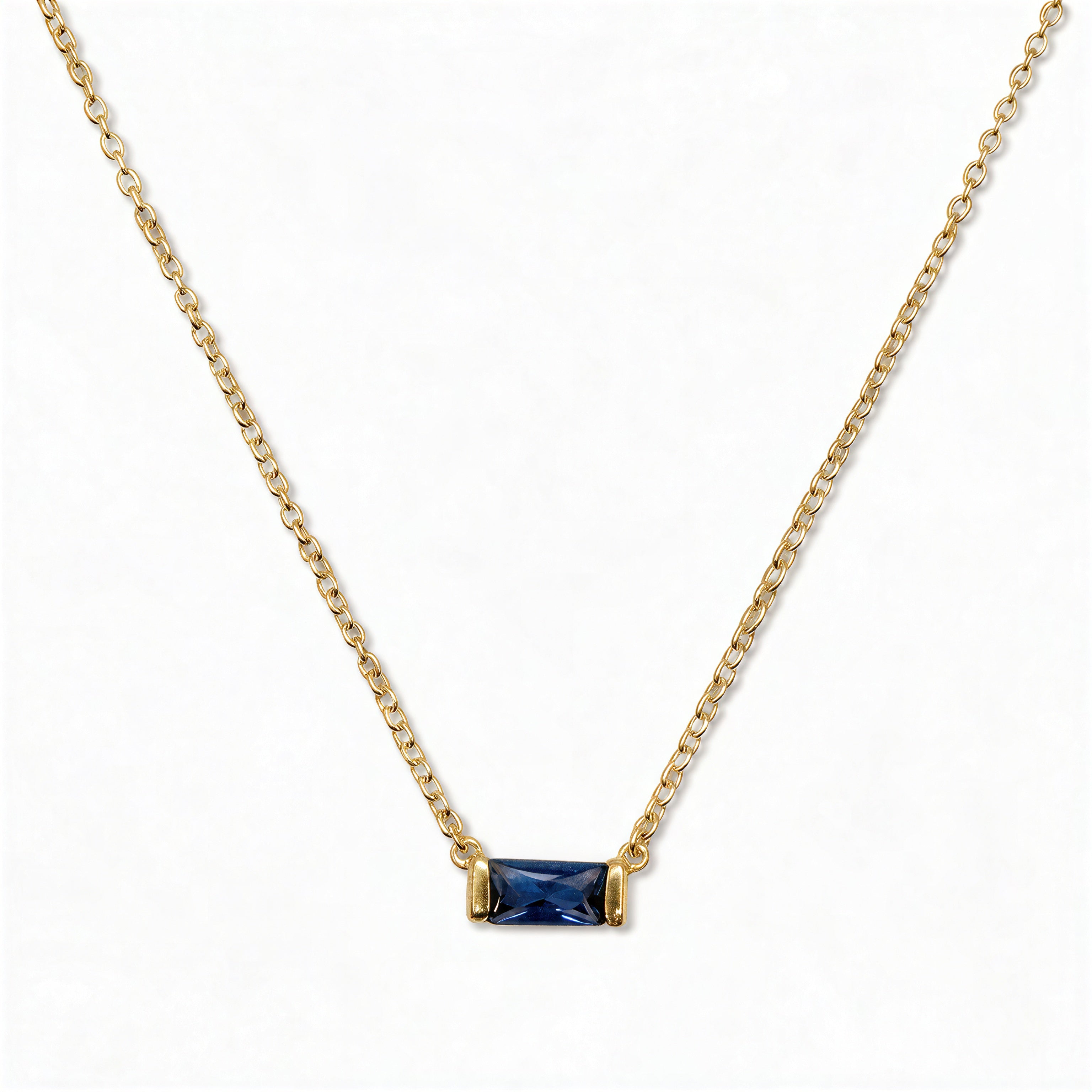 A September Birthstone Sapphire Cubic Zirconia Baguette Necklace by Skōsh Jewelry, featuring a slim rectangular deep blue baguette stone set horizontally on a fine gold chain, displayed against a white background.