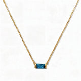 A December Birthstone Aqua Cubic Zirconia Baguette Necklace by Skōsh Jewelry, featuring a slim rectangular blue baguette stone set horizontally on a fine gold chain, displayed against a white background.