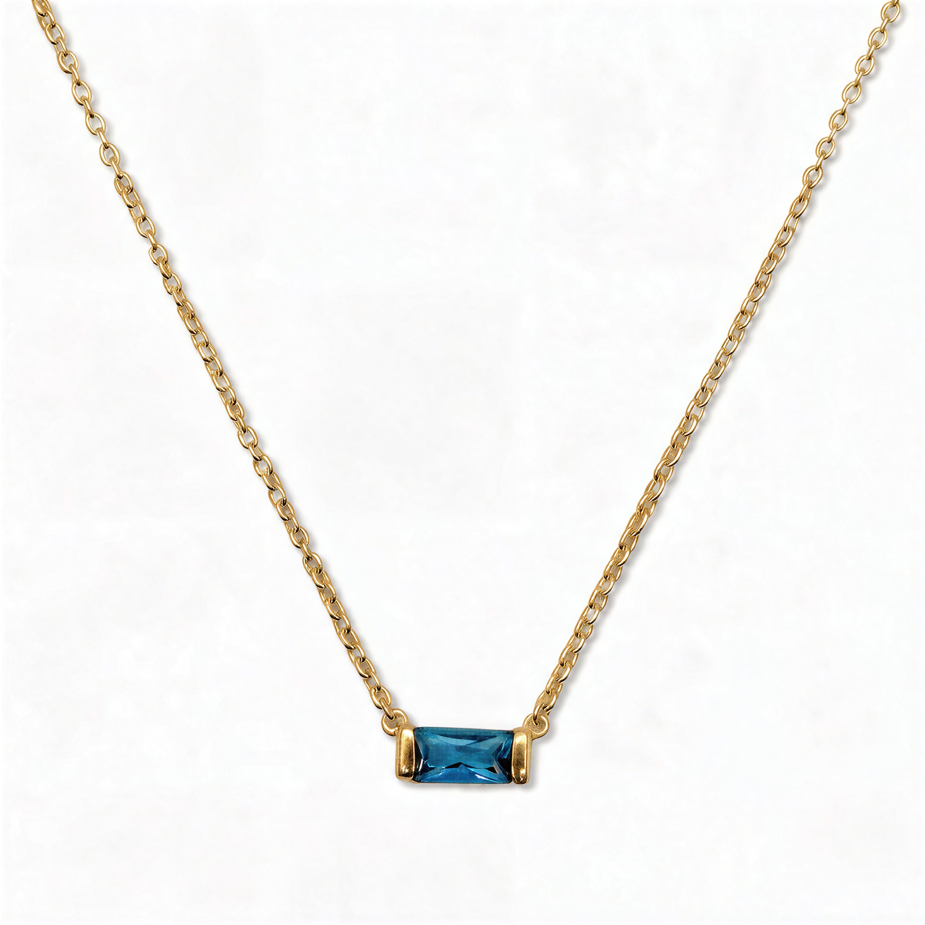 A December Birthstone Aqua Cubic Zirconia Baguette Necklace by Skōsh Jewelry, featuring a slim rectangular blue baguette stone set horizontally on a fine gold chain, displayed against a white background.