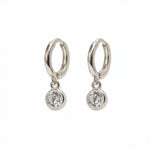 A pair of Bezel Set White Cubic Zirconia Drop Huggie Hoop Earrings by Skōsh Jewelry, featuring small sterling silver huggie hoops, each with a round bezel-set clear stone dangling below, displayed against a white background.