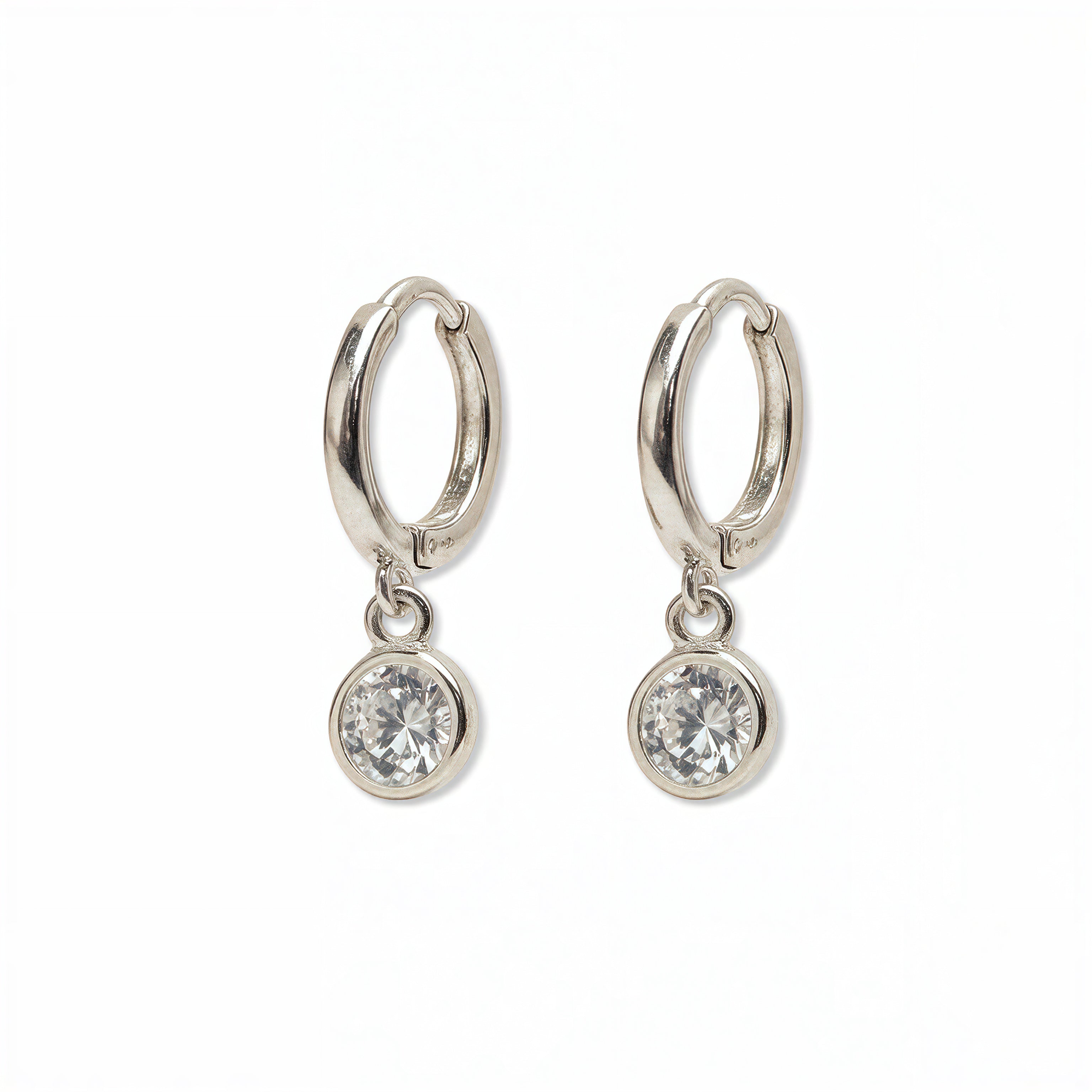 A pair of Bezel Set White Cubic Zirconia Drop Huggie Hoop Earrings by Skōsh Jewelry, featuring small sterling silver huggie hoops, each with a round bezel-set clear stone dangling below, displayed against a white background.