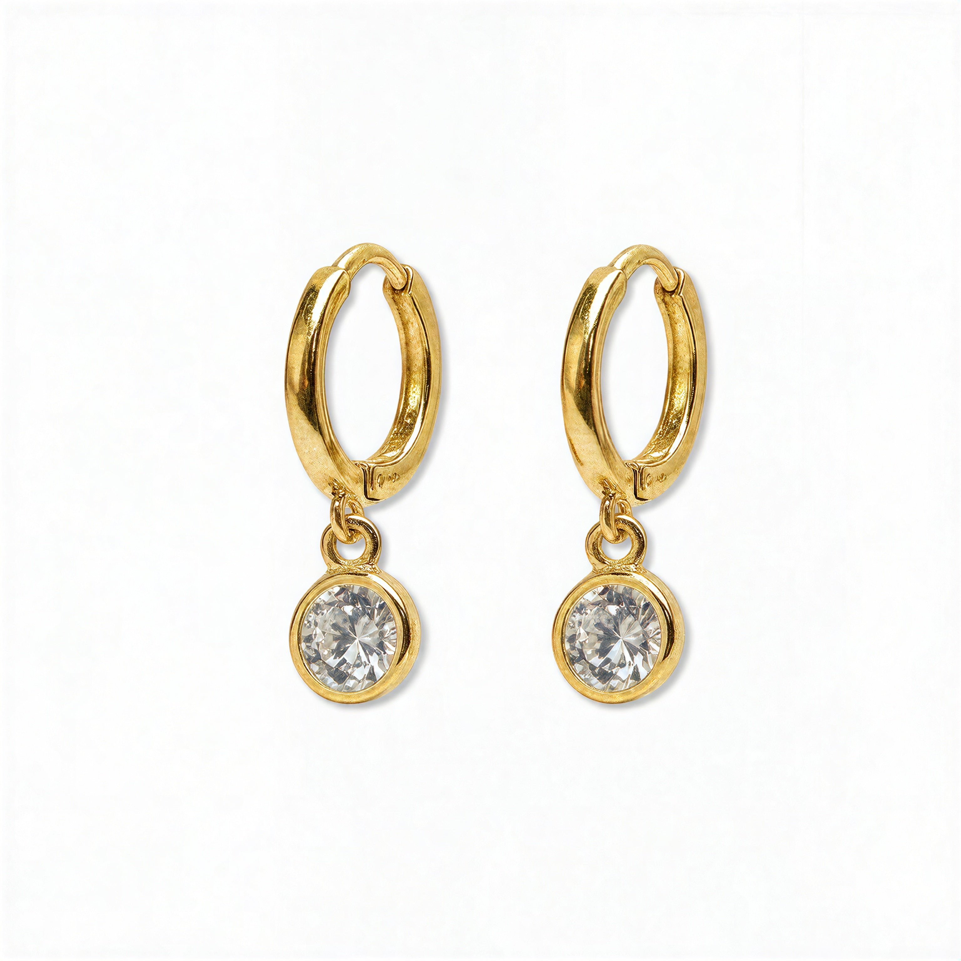 A pair of Bezel Set White Cubic Zirconia Drop Huggie Hoop Earrings by Skōsh Jewelry, featuring small gold huggie hoops, each with a round bezel-set clear stone dangling below, displayed against a white background.