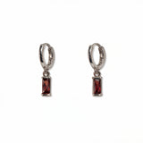 A pair of January Birthstone Garnet Cubic Zirconia Baguette Earrings by Skōsh Jewelry, featuring small sterling silver huggie hoops, each with a rectangular deep red baguette stone dangling below, displayed against a white background.