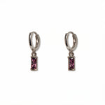 A pair of February Birthstone Amethyst Cubic Zirconia Baguette Earrings by Skōsh Jewelry, featuring small sterling silver huggie hoops, each with a rectangular purple baguette stone dangling below, displayed against a white background.