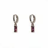 A pair of February Birthstone Amethyst Cubic Zirconia Baguette Earrings by Skōsh Jewelry, featuring small sterling silver huggie hoops, each with a rectangular purple baguette stone dangling below, displayed against a white background.