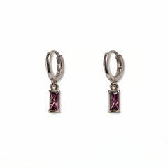 A pair of February Birthstone Amethyst Cubic Zirconia Baguette Earrings by Skōsh Jewelry, featuring small sterling silver huggie hoops, each with a rectangular purple baguette stone dangling below, displayed against a white background.