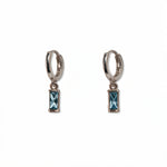 A pair of March Birthstone Light Sapphire Cubic Zirconia Baguette Earrings by Skōsh Jewelry, featuring small sterling silver huggie hoops, each with a rectangular light blue baguette stone dangling below, displayed against a white background.