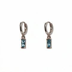 A pair of March Birthstone Light Sapphire Cubic Zirconia Baguette Earrings by Skōsh Jewelry, featuring small sterling silver huggie hoops, each with a rectangular light blue baguette stone dangling below, displayed against a white background.
