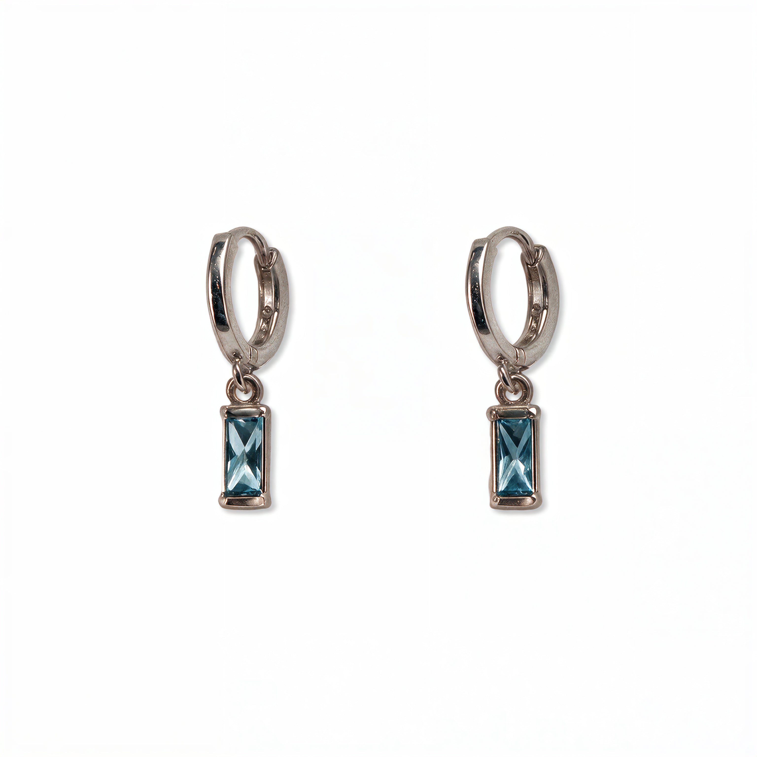 A pair of March Birthstone Light Sapphire Cubic Zirconia Baguette Earrings by Skōsh Jewelry, featuring small sterling silver huggie hoops, each with a rectangular light blue baguette stone dangling below, displayed against a white background.