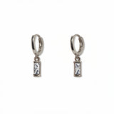 A pair of April Birthstone White Cubic Zirconia Baguette Earrings by Skōsh Jewelry, featuring small sterling silver huggie hoops, each with a rectangular clear baguette stone dangling below, displayed against a white background.