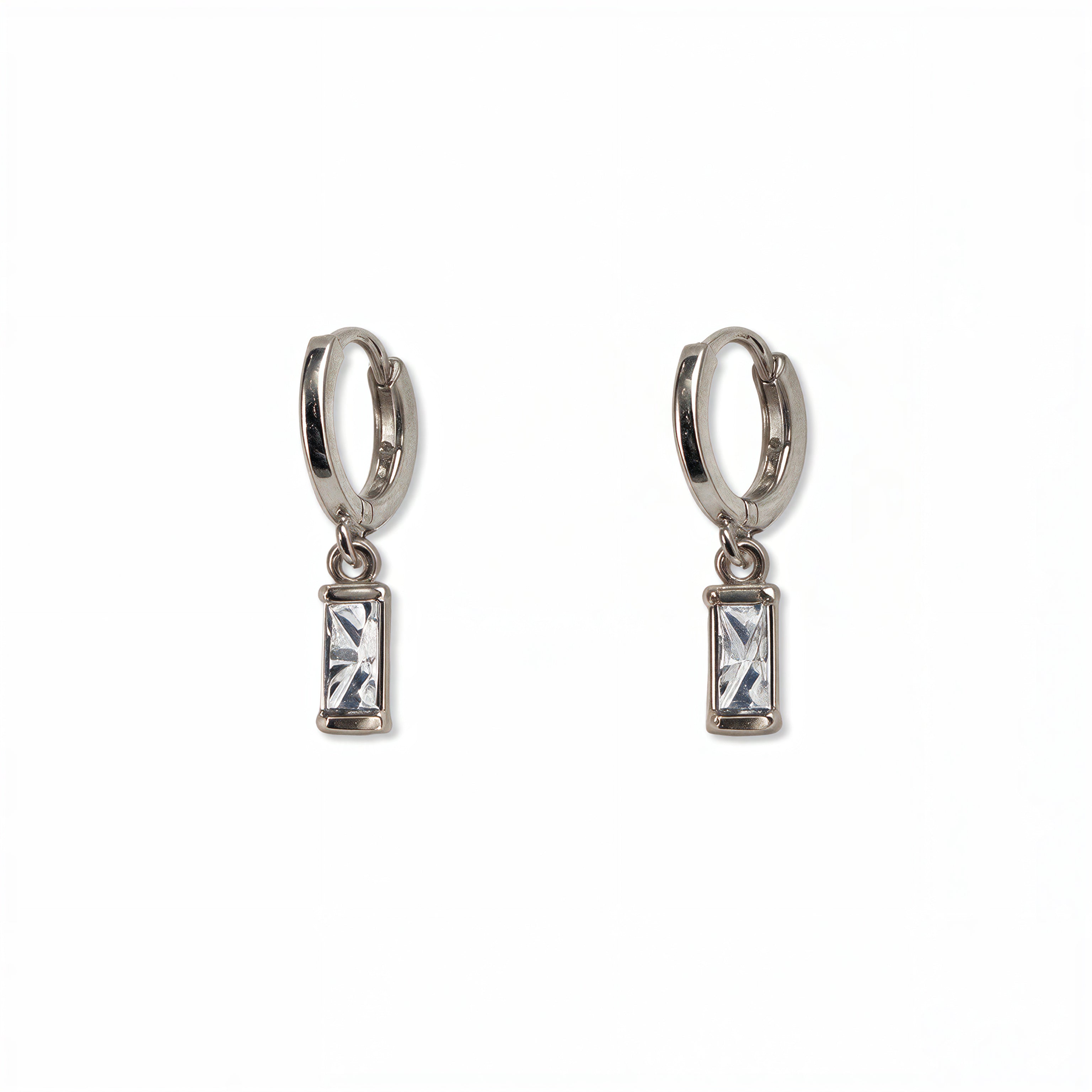 A pair of April Birthstone White Cubic Zirconia Baguette Earrings by Skōsh Jewelry, featuring small sterling silver huggie hoops, each with a rectangular clear baguette stone dangling below, displayed against a white background.