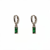 A pair of May Birthstone Emerald Cubic Zirconia Baguette Earrings by Skōsh Jewelry, featuring small sterling silver huggie hoops, each with a rectangular green baguette stone dangling below, displayed against a white background.