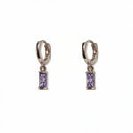 A pair of June Birthstone Lavender Cubic Zirconia Baguette Earrings by Skōsh Jewelry, featuring small sterling silver huggie hoops, each with a rectangular light purple baguette stone dangling below, displayed against a white background.