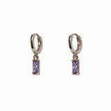 A pair of June Birthstone Lavender Cubic Zirconia Baguette Earrings by Skōsh Jewelry, featuring small sterling silver huggie hoops, each with a rectangular light purple baguette stone dangling below, displayed against a white background.