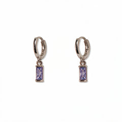 A pair of June Birthstone Lavender Cubic Zirconia Baguette Earrings by Skōsh Jewelry, featuring small sterling silver huggie hoops, each with a rectangular light purple baguette stone dangling below, displayed against a white background.