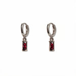 A pair of July Birthstone Ruby Cubic Zirconia Baguette Earrings by Skōsh Jewelry, featuring small sterling silver huggie hoops, each with a rectangular red baguette stone dangling below, displayed against a white background.