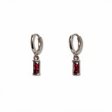 A pair of July Birthstone Ruby Cubic Zirconia Baguette Earrings by Skōsh Jewelry, featuring small sterling silver huggie hoops, each with a rectangular red baguette stone dangling below, displayed against a white background.