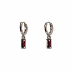 A pair of July Birthstone Ruby Cubic Zirconia Baguette Earrings by Skōsh Jewelry, featuring small sterling silver huggie hoops, each with a rectangular red baguette stone dangling below, displayed against a white background.