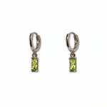 A pair of August Birthstone Peridot Cubic Zirconia Baguette Earrings by Skōsh Jewelry, featuring small sterling silver huggie hoops, each with a rectangular light green baguette stone dangling below, displayed against a white background.