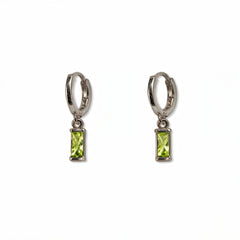 A pair of August Birthstone Peridot Cubic Zirconia Baguette Earrings by Skōsh Jewelry, featuring small sterling silver huggie hoops, each with a rectangular light green baguette stone dangling below, displayed against a white background.