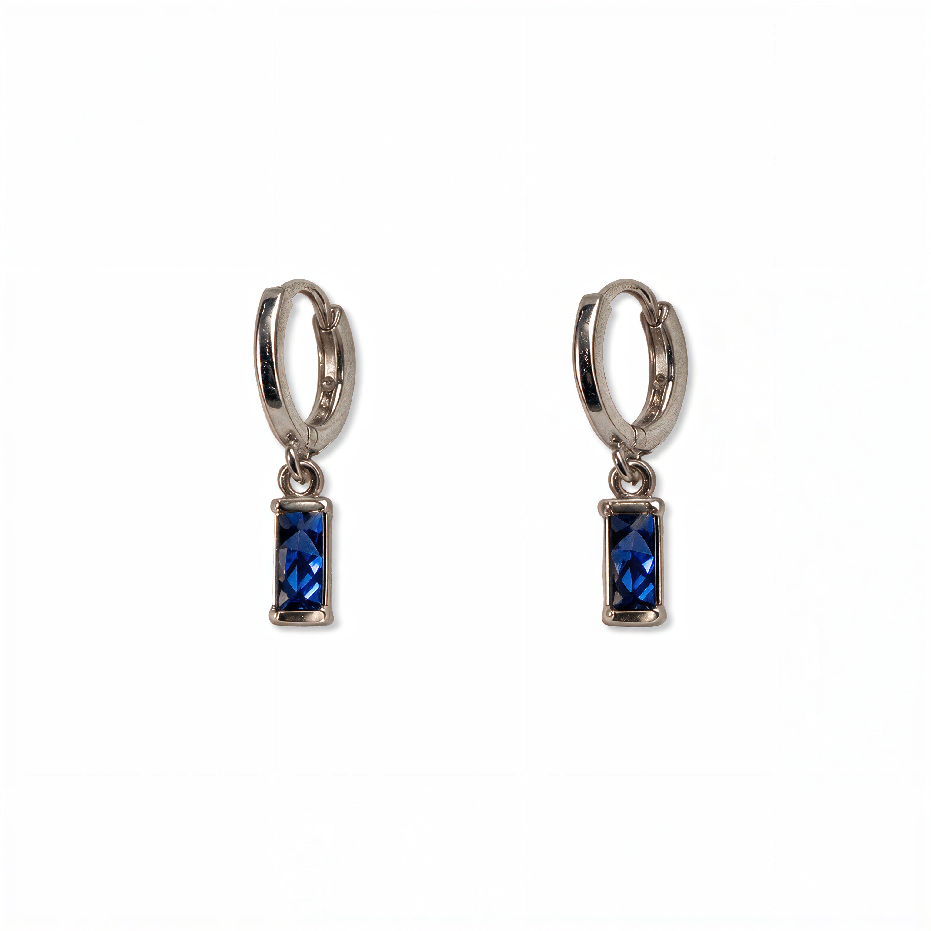 A pair of September Birthstone Sapphire Cubic Zirconia Baguette Earrings by Skōsh Jewelry, featuring small sterling silver huggie hoops, each with a rectangular deep blue baguette stone dangling below, displayed against a white background.