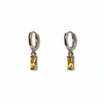 A pair of November Birthstone Citrine Cubic Zirconia Baguette Earrings by Skōsh Jewelry, featuring small sterling silver huggie hoops, each with a rectangular yellow baguette stone dangling below, displayed against a white background.