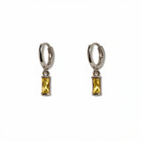 A pair of November Birthstone Citrine Cubic Zirconia Baguette Earrings by Skōsh Jewelry, featuring small sterling silver huggie hoops, each with a rectangular yellow baguette stone dangling below, displayed against a white background.