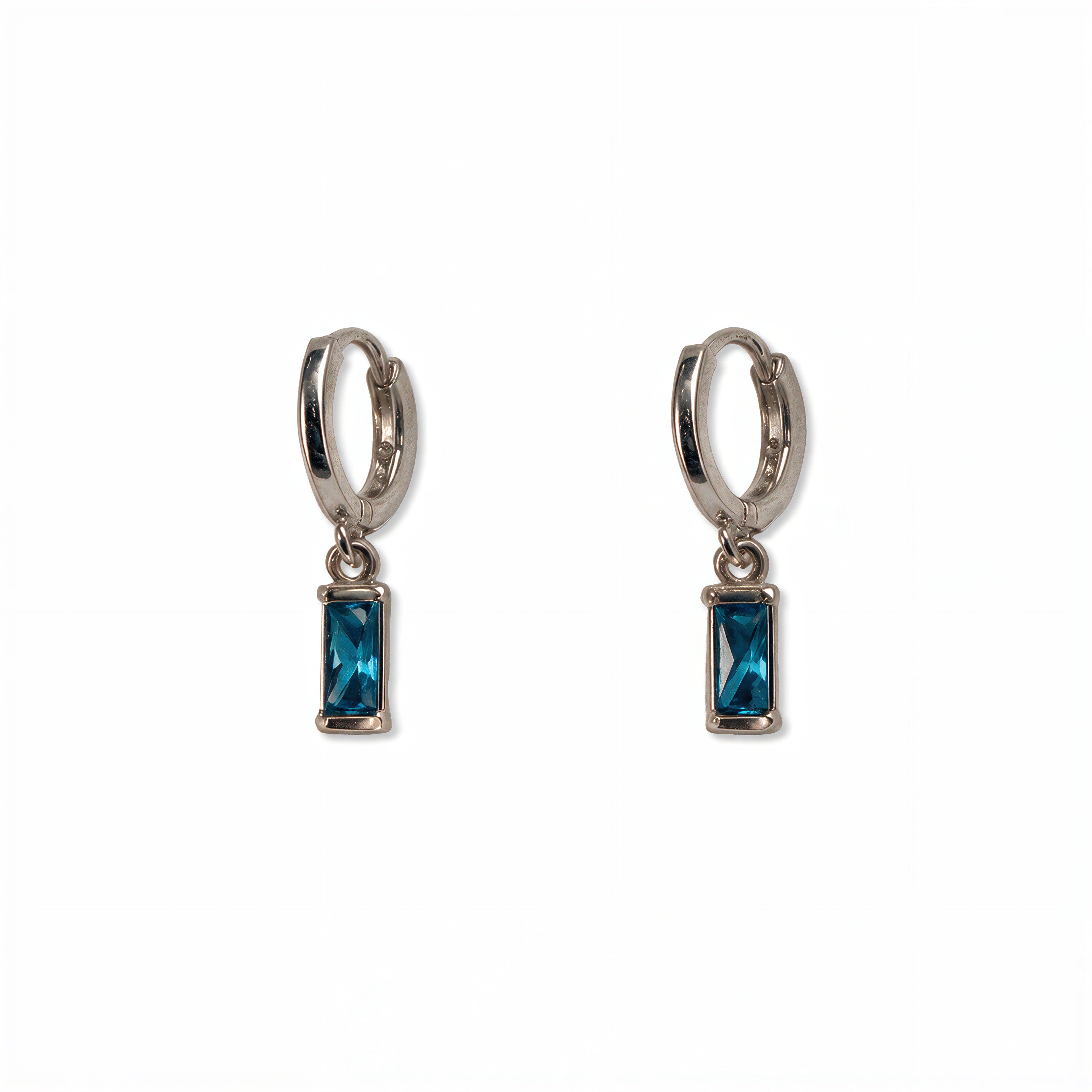 A pair of December Birthstone Aqua Cubic Zirconia Baguette Earrings by Skōsh Jewelry, featuring small sterling silver huggie hoops, each with a rectangular blue baguette stone dangling below, displayed against a white background.