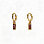 A pair of January Birthstone Garnet Cubic Zirconia Baguette Earrings by Skōsh Jewelry, featuring small gold huggie hoops, each with a rectangular deep red baguette stone dangling below, displayed against a white background.