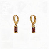 A pair of January Birthstone Garnet Cubic Zirconia Baguette Earrings by Skōsh Jewelry, featuring small gold huggie hoops, each with a rectangular deep red baguette stone dangling below, displayed against a white background.