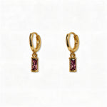 A pair of February Birthstone Amethyst Cubic Zirconia Baguette Earrings by Skōsh Jewelry, featuring small gold huggie hoops, each with a rectangular purple baguette stone dangling below, displayed against a white background.
