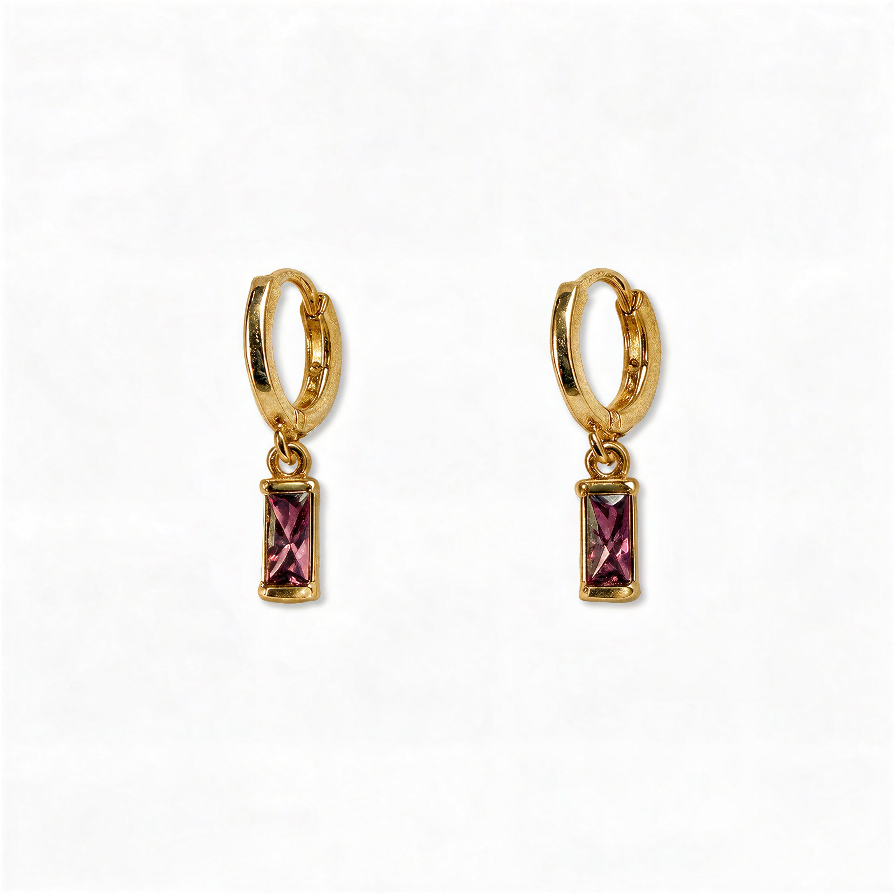 A pair of February Birthstone Amethyst Cubic Zirconia Baguette Earrings by Skōsh Jewelry, featuring small gold huggie hoops, each with a rectangular purple baguette stone dangling below, displayed against a white background.