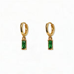 A pair of May Birthstone Emerald Cubic Zirconia Baguette Earrings by Skōsh Jewelry, featuring small gold huggie hoops, each with a rectangular green baguette stone dangling below, displayed against a white background.