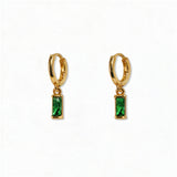 A pair of May Birthstone Emerald Cubic Zirconia Baguette Earrings by Skōsh Jewelry, featuring small gold huggie hoops, each with a rectangular green baguette stone dangling below, displayed against a white background.