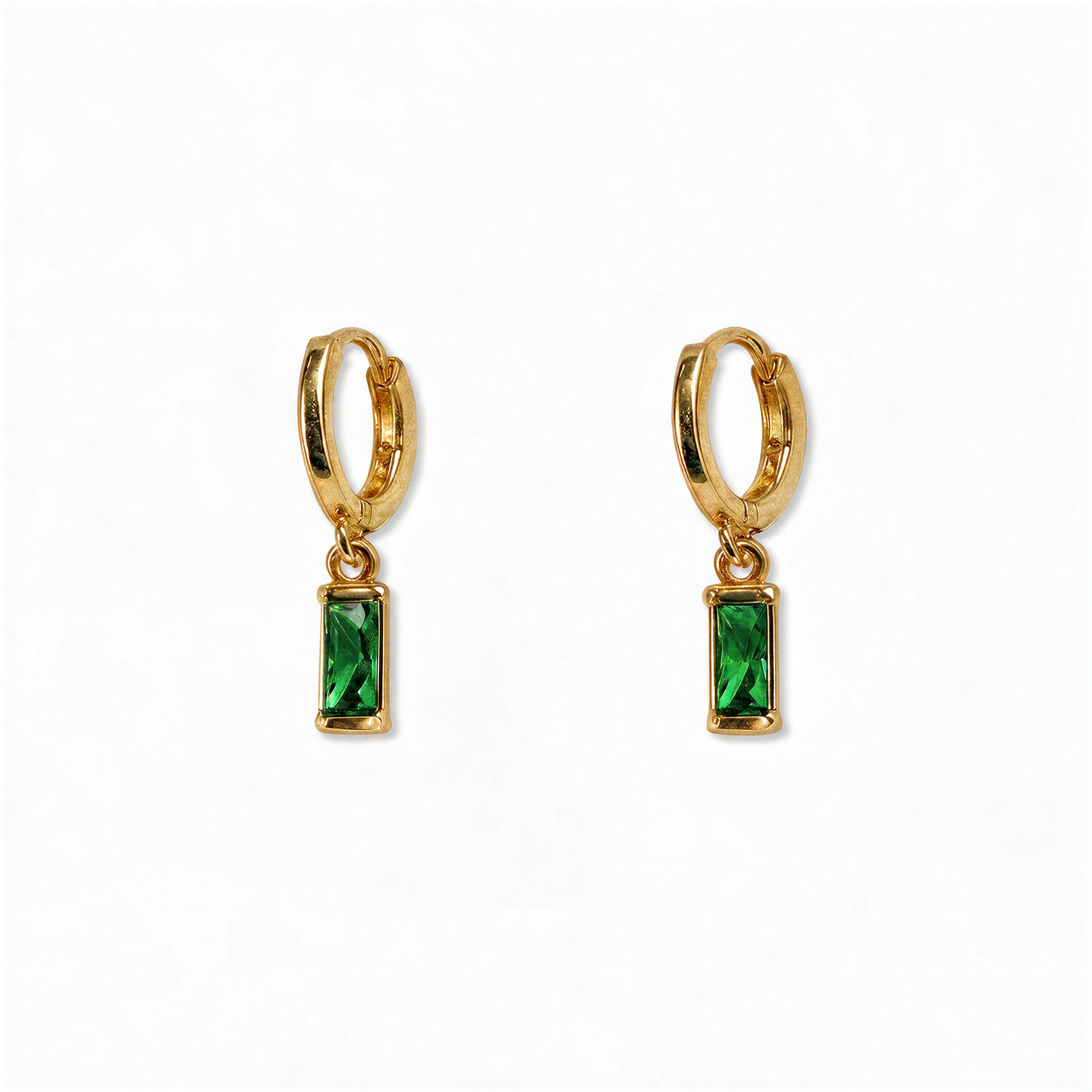 A pair of May Birthstone Emerald Cubic Zirconia Baguette Earrings by Skōsh Jewelry, featuring small gold huggie hoops, each with a rectangular green baguette stone dangling below, displayed against a white background.
