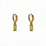 A pair of August Birthstone Peridot Cubic Zirconia Baguette Earrings by Skōsh Jewelry, featuring small gold huggie hoops, each with a rectangular light green baguette stone dangling below, displayed against a white background.